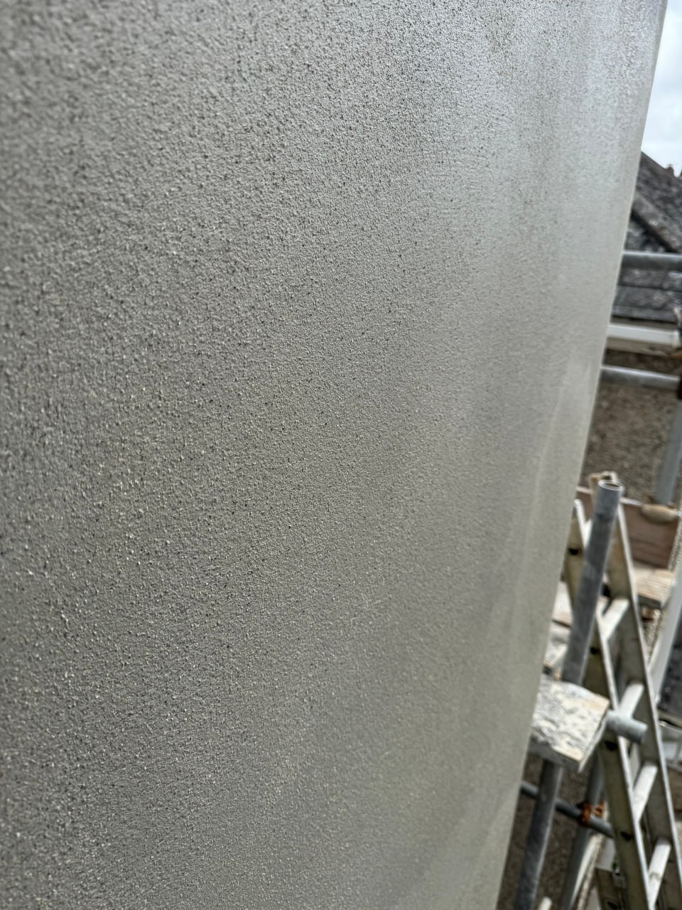 A close-up view of a freshly applied grey cement render finish on an external wall under construction with scaffolding in Cornwall.