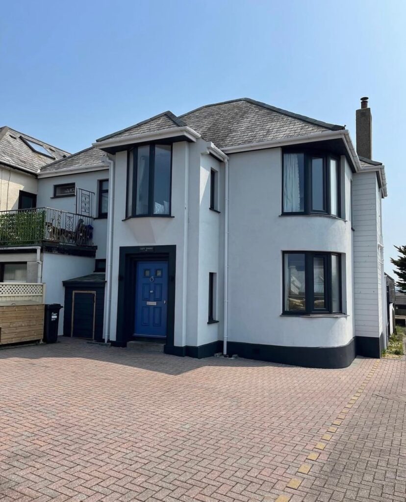 A freshly completed white K-rend plaster finish on a two-story detached house with contrasting black window frames and a blue front door in Cornwall.