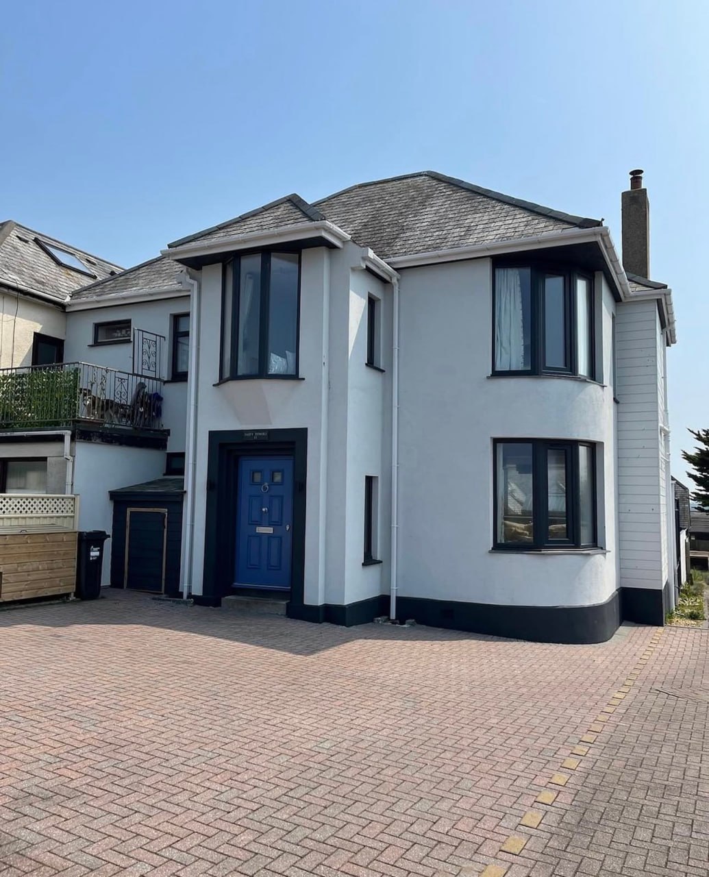 A freshly completed white K-rend plaster finish on a two-story detached house with contrasting black window frames and a blue front door in Cornwall.