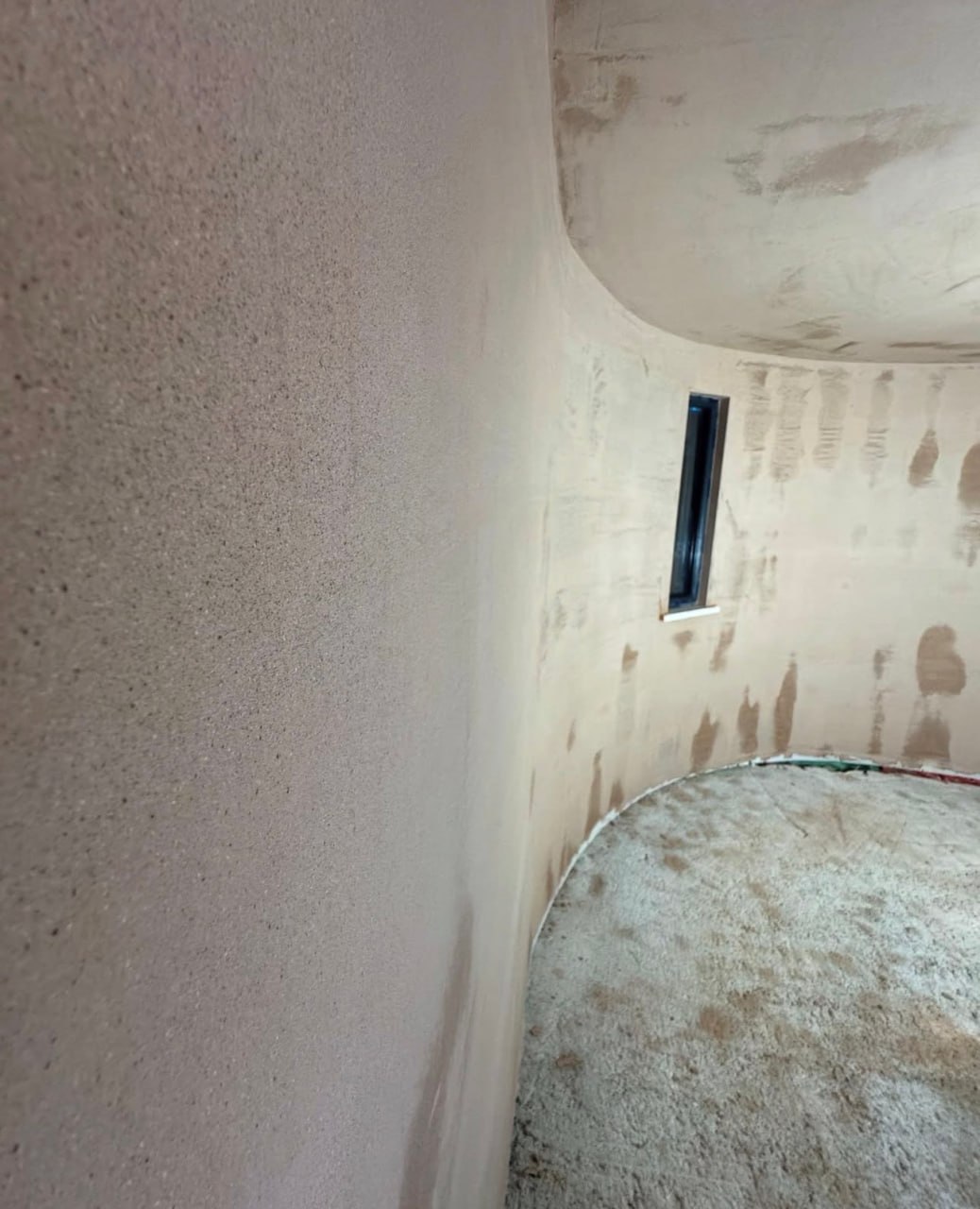 Hand-applied lime plaster on a unique curved interior wall with a narrow window under construction in Cornwall.
