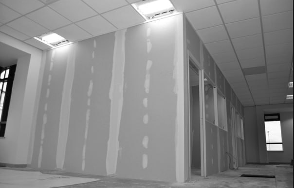 Interior view of a commercial office space under construction, showing newly installed plasterboard walls with joint compound tape and a grid drop ceiling in Cornwall.